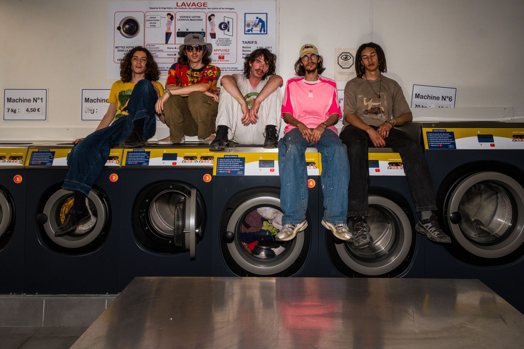 Les cinq membres de SuperMegaSuperCool Révolution assis sur les machines d’une laverie